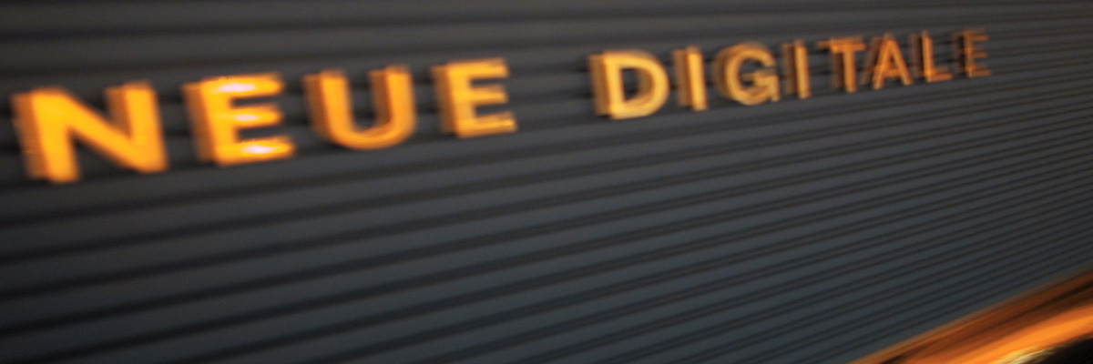 Schriftzug „Neue Digitale“ in orangefarbenen Buchstaben an einer dunklen Wand der Agentur